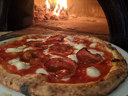 A freshly baked pizza with pepperoni and mozzarella, placed in front of a wood-fired oven.