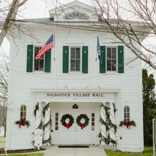 Saugatuck Village Hall, a white building with green shutters, decorated with wreaths and flags for the holiday season.