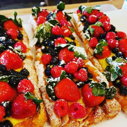 Three pastry desserts topped with strawberries, raspberries, blueberries, and powdered sugar on a white plate.