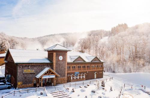 A cozy wooden lodge in a snowy landscape, surrounded by trees and mist, with a clock tower and clear blue sky.