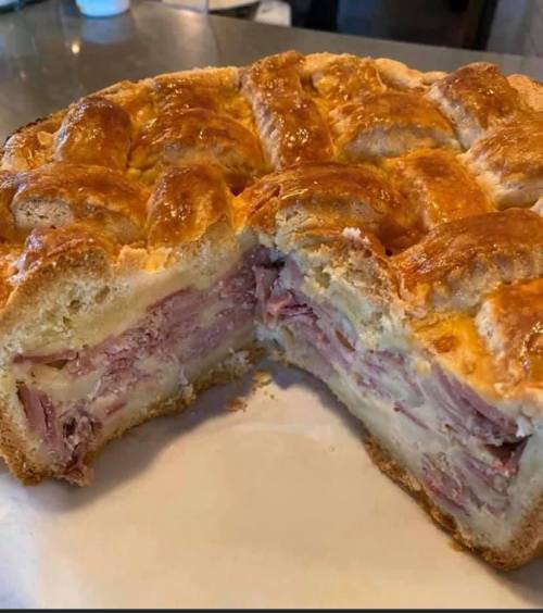 A freshly baked pie with a golden crust, filled with layers of ham and cheese, with a slice cut out to reveal the filling.