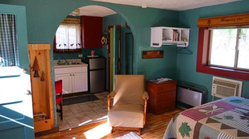 Cozy room with a chair, kitchenette, and a bed, featuring colorful decor and natural light from a window.