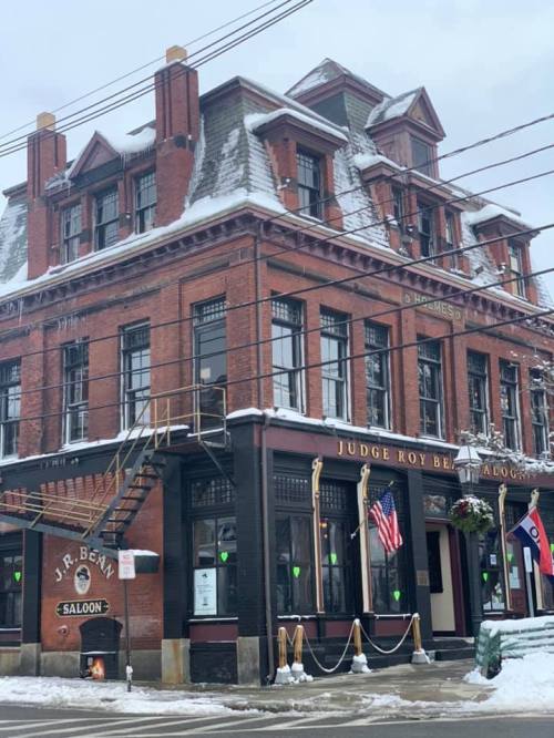 Historic brick building with snow on the roof, featuring a saloon and festive decorations, including flags and wreaths.