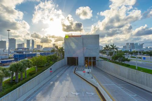 A modern concrete structure with a sunlit sky, palm trees, and city skyline in the background.
