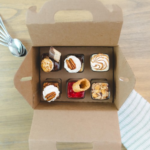 A cardboard box containing six assorted desserts, including mini cakes and cream-topped treats.