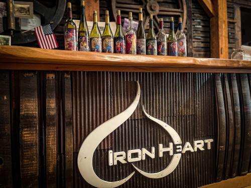 A wooden bar with the "Iron Heart" logo, displaying various wine bottles with colorful labels and an American flag.