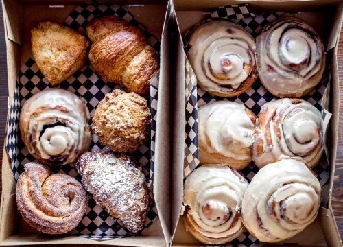 Two boxes of assorted pastries: croissants, cinnamon rolls, scones, and sweet rolls, arranged on checkered paper.