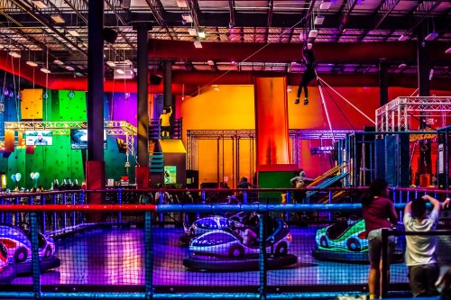 A vibrant indoor amusement center with bumper cars, climbing walls, and colorful lighting.