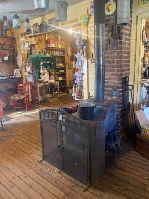 A vintage wood stove in a rustic shop, surrounded by wooden floors and various nostalgic decor items.