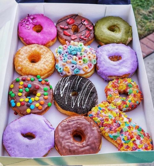 A box of colorful donuts, featuring various toppings like sprinkles, cereal, and icing in vibrant shades.
