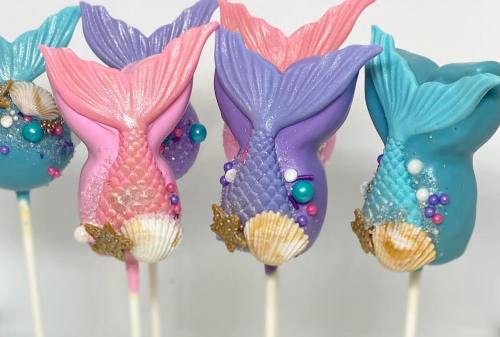 Colorful mermaid tail cake pops decorated with shells and pearls, featuring pink, purple, and blue hues.