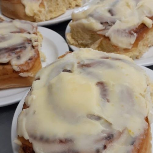 Close-up of fluffy cinnamon rolls topped with creamy white icing on white plates.