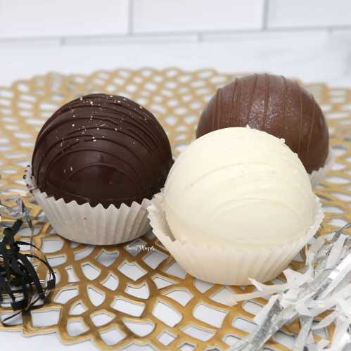 Three decorative chocolate spheres in dark, milk, and white chocolate on a lace-like gold doily.