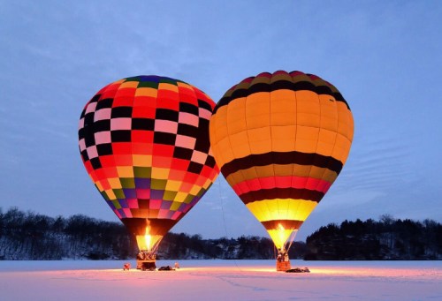 Two colorful hot air balloons glow against a twilight sky, set on a snowy landscape.