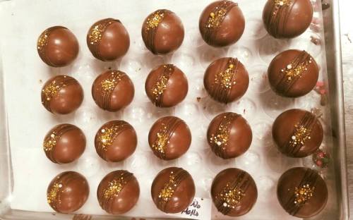 A tray of chocolate-covered truffles decorated with gold sprinkles and drizzled chocolate.