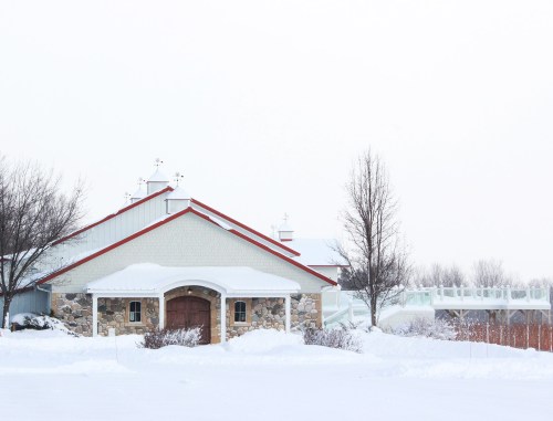 A snow-covered building with a stone facade and a red roof, surrounded by a winter landscape.