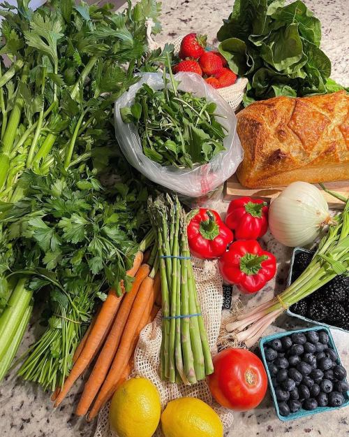 A variety of fresh vegetables and fruits, including celery, strawberries, peppers, carrots, and bread on a countertop.