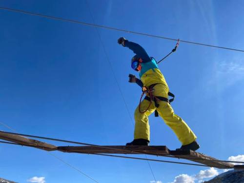 A person in bright yellow and blue gear balances on a high wire against a clear blue sky.
