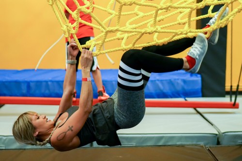 A woman hangs from a rope net in a gym, wearing athletic gear and focused on her workout.
