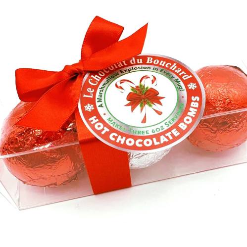 A clear box containing three hot chocolate bombs wrapped in red and silver foil, tied with a red ribbon.