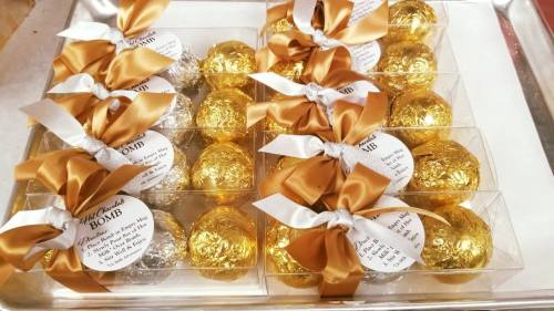 A tray of decorative bath bombs wrapped in gold and silver foil, tied with elegant ribbons and tags.