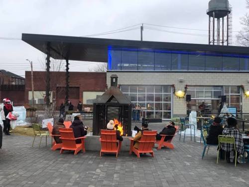 People sitting around a fire pit in colorful chairs, enjoying a chilly day at an outdoor gathering space.