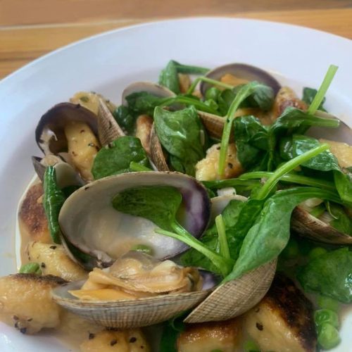 A plate of gnocchi with clams and fresh spinach, garnished with green onions in a light sauce.