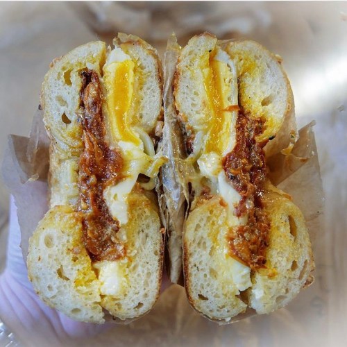 A close-up of a sandwich cut in half, featuring melted cheese, egg, and a crispy filling in a toasted bun.