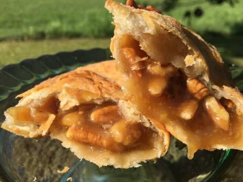 Close-up of a flaky pastry filled with caramel and pecans, displayed on a glass plate with a green background.