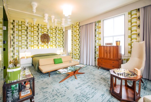 A stylish retro bedroom featuring green wallpaper, a modern bed, a chess set, and mid-century furniture.