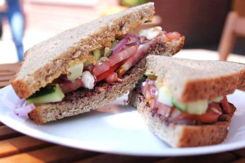 A close-up of a sandwich with layers of vegetables, including tomatoes, cucumbers, and onions, on whole grain bread.