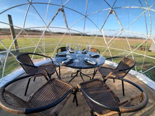A clear dome structure with a table set for dining, surrounded by chairs and a scenic outdoor view.