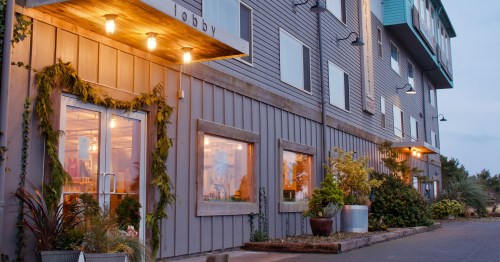 Exterior view of a modern building with a lobby entrance, large windows, and greenery along the facade at dusk.