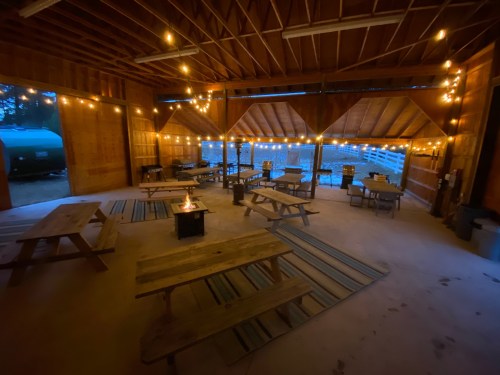 Cozy indoor space with wooden tables, string lights, and a fire pit, overlooking a serene outdoor area.