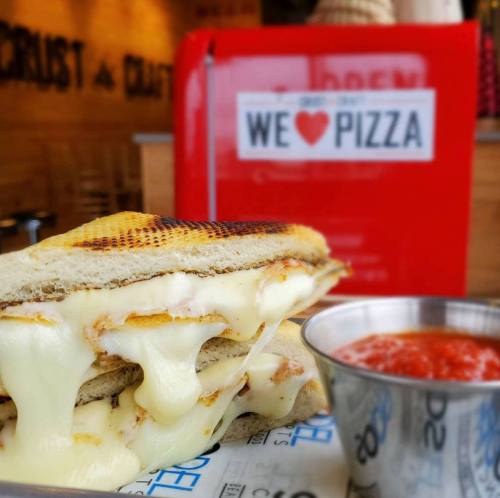 A grilled cheese sandwich with melted cheese, served with a side of marinara sauce, against a pizza-themed backdrop.