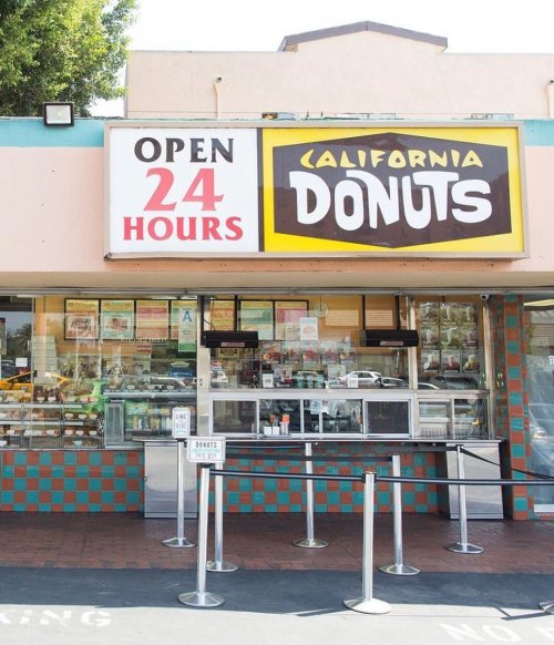 A storefront of California Donuts, open 24 hours, featuring a large sign and a service window with a queue.