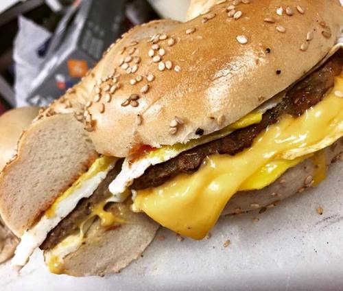 A close-up of a sesame seed bagel sandwich filled with cheese, egg, and sausage patty.