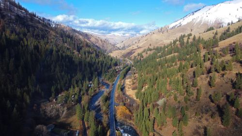 Aerial view of a winding river surrounded by lush green forests and rolling hills under a blue sky with scattered clouds.