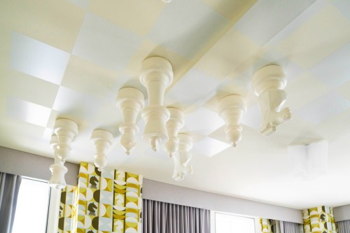 Ceiling featuring oversized white chess pieces and a patterned wall in a modern interior design.