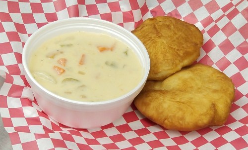 A bowl of creamy soup with vegetables, accompanied by two golden-brown fried pastries on a red-checkered paper.