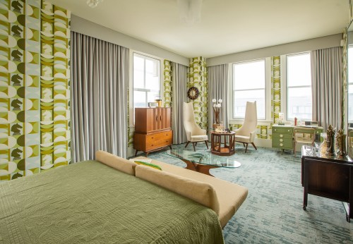 A stylish retro bedroom featuring patterned wallpaper, a green bedspread, and mid-century furniture.