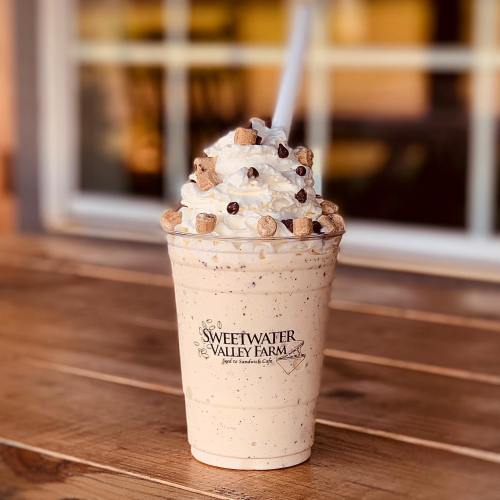 A creamy milkshake topped with whipped cream, chocolate chips, and crunchy bits, served in a branded cup.