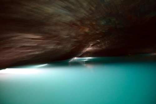 A blurred underwater scene with turquoise water and a dark rocky overhang above.