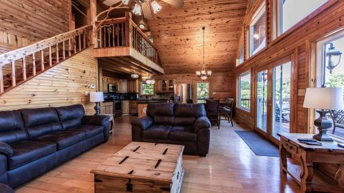 Cozy wooden cabin interior featuring leather sofas, a wooden coffee table, and large windows with natural light.