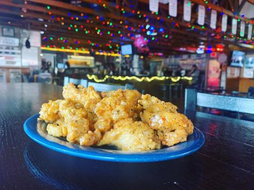 A blue plate of golden, crispy chicken wings sits on a table, with a colorful, festive background of lights.