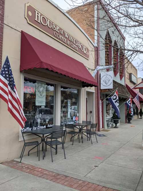 Exterior of House of Windsor Coffee & Gifts, featuring outdoor seating and American flags, on a charming street.