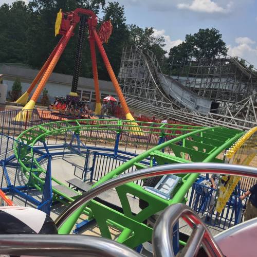 A colorful amusement park scene featuring a roller coaster and a thrill ride under a blue sky.
