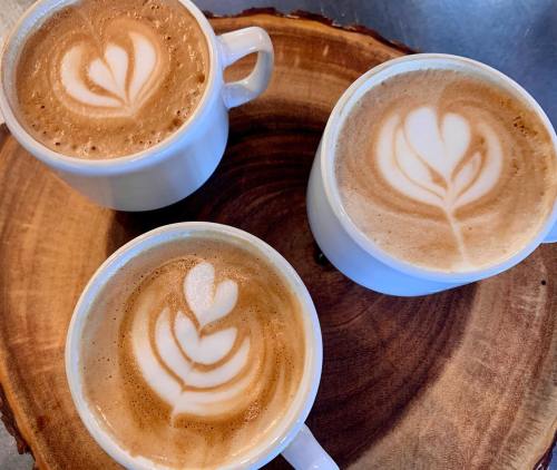 Three cups of coffee with latte art, featuring heart and leaf designs, arranged on a wooden serving platter.