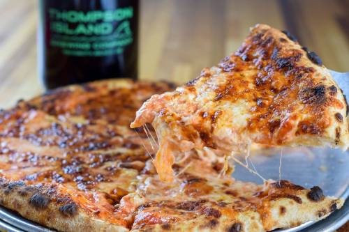 A slice of cheesy pizza being lifted from a round pizza, with a bottle in the background.