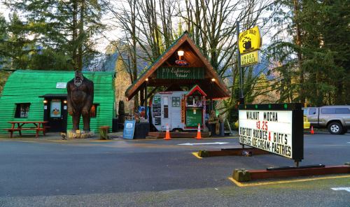 A quirky roadside stand with a large gorilla statue, serving coffee and gifts, surrounded by trees and mountains.